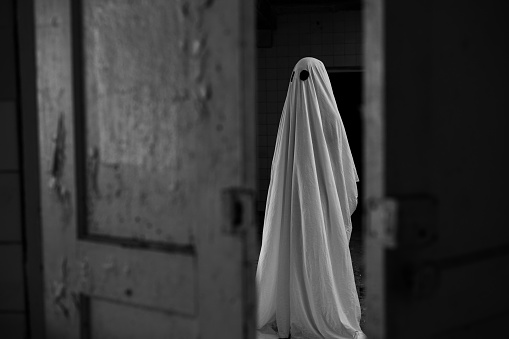 Ghost in a white sheet walking in an abandoned old house at night. Copy space