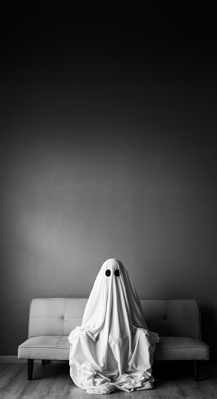 Black and white photo of a ghost sitting on the couch in house, portrait of a kind ghost. Banner. Copy space