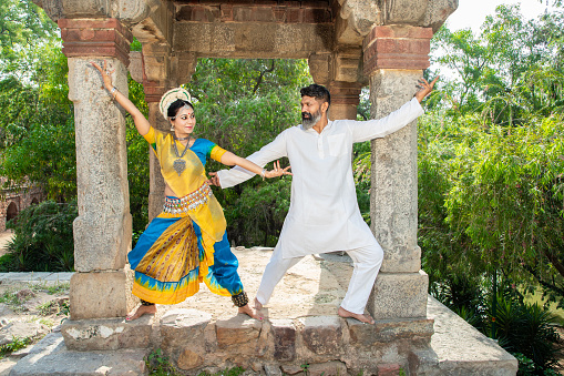 Indian woman Odissi dancer doing classical dance along with teacher or master outdoor. female do Orissi dance traning with coach. art and culture of india.