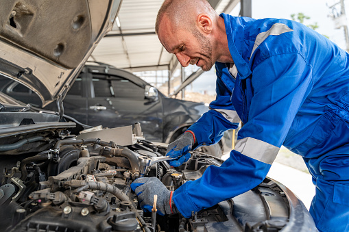 A male car mechanic in blue jumpsuit working hard to repair the car engine at his car repair garage