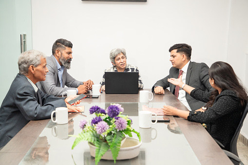 Group of businessmen and businesswomen sitting and talking at a table with laptops during a board meeting.