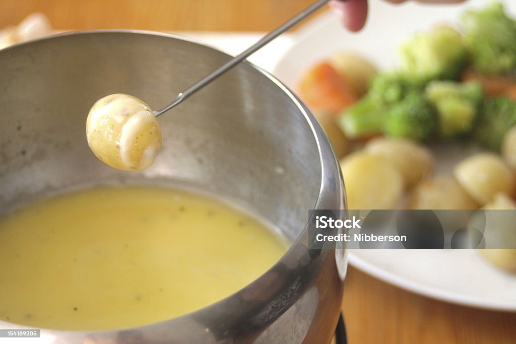 Cheese Fondue Cheese coated potato positioned alluringly over bubbling cheese fondue. Selection of dipping vegetables in background. Jarlsberg Stock Photo