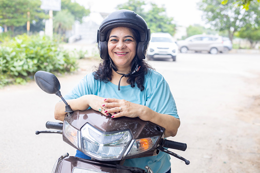 Happy mature woman wearing helmet sitting on motor bike or scooter with the smile on his face.