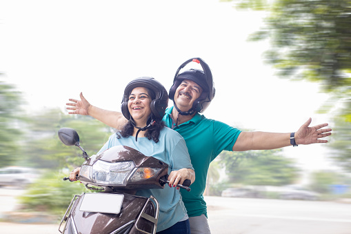 Happy senior indian couple wearing helmet riding motor scooter on road. Retirement life, Adventure and travel, Closeup