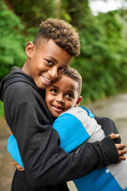 Portrait of two young boys hugging each other standing outside and looking at camera