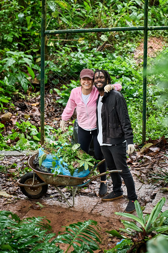 Portrait of two happy male and female volunteers with garbage wheelbarrow in front looking at camera during a community cleanup day in garden