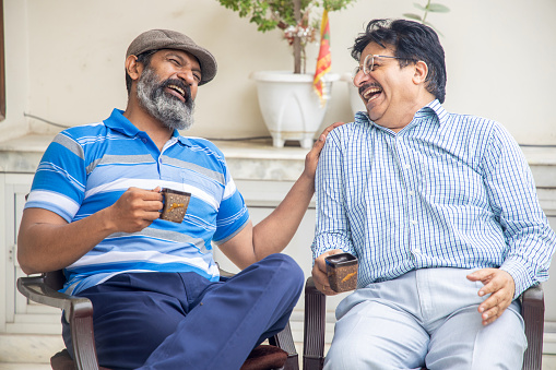 Happy indian mature friends enjoying morning tea or coffee together. Domestic or retirement life.