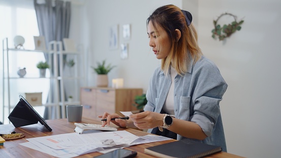 Woman calculates on calculator for personal finance,paysckeck paper receipt expense biil statement,planning budgets of monthly personal balance at home.