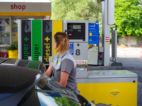 Cremona, Italy - July 3 2023 caucasian service woman at Eni Agip city fuel station pumping petrol to a customer car