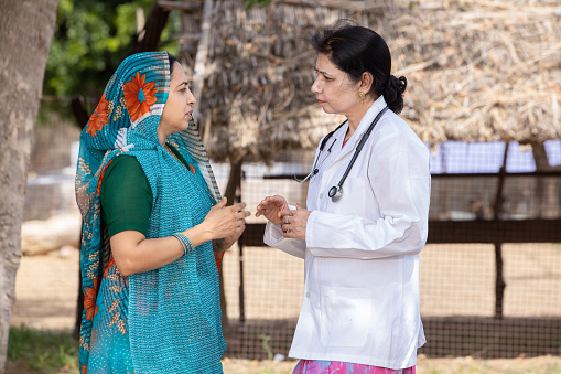 Indian female doctor with traditional woman wearing sari  in village consulting outdoor, Rural India healthcare concept.