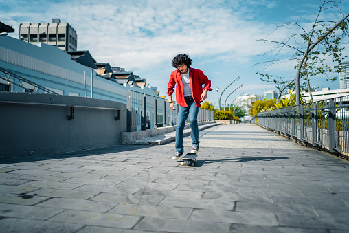 Asian Malay young man practicing skateboarding at pedestrian walkway during weekend morning