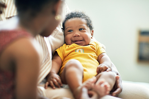 Over the shoulder view with focus on 2 month old Black infant lying in mother’s arm, face to face with 6 year old sibling and showing positive emotion.