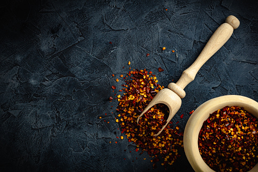 Top view red dried crushed hot chili peppers and chili flakes or powder in wooden spoon and bowl on grey rustic background, healthy turkish spice