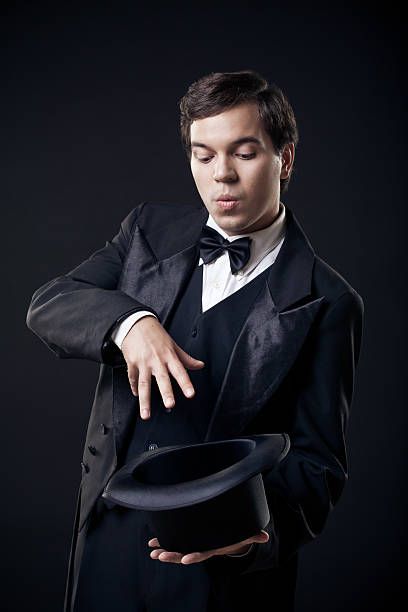 magician showing tricks with top hat isolated on dark background magician showing tricks with top hat isolated on dark background tail coat photos stock pictures, royalty-free photos & images
