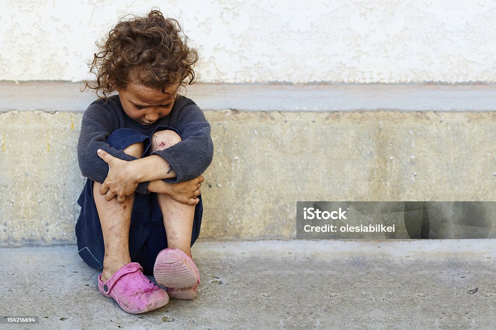 poor, sad little child girl sitting against the concrete wall Child Stock Photo