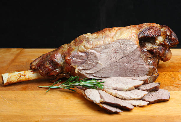 Roast leg of lamb sliced on a wooden board with rosemary Roast leg of lamb on wooden carving board. Visible steam rising. animal leg stock pictures, royalty-free photos & images