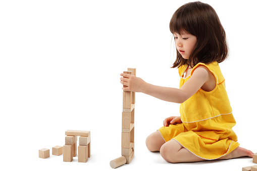 A little girl playing with wooden blocks on the table in playroom.  Educational game for baby and toddler in modern nursery. The kid builds a tower from wooden rainbow stacking blocks.