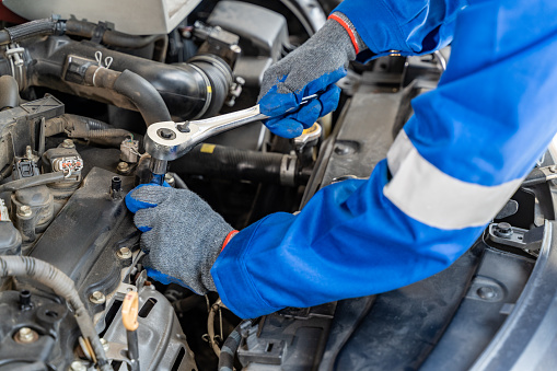 Close up hands of a male car mechanic using retchet wrench while working on the car's engine