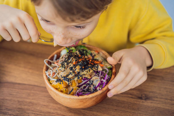 Boy eating Raw Organic Poke Bowl with Rice and Veggies close-up on the table. Top view from above horizontal Boy eating Raw Organic Poke Bowl with Rice and Veggies close-up on the table. Top view from above horizontal. kids eating tuna stock pictures, royalty-free photos & images
