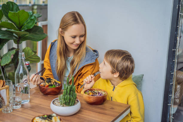 Mother and son eating Raw Organic Poke Bowl with Rice and Veggies close-up on the table. Top view from above horizontal Mother and son eating Raw Organic Poke Bowl with Rice and Veggies close-up on the table. Top view from above horizontal. kids eating tuna stock pictures, royalty-free photos & images