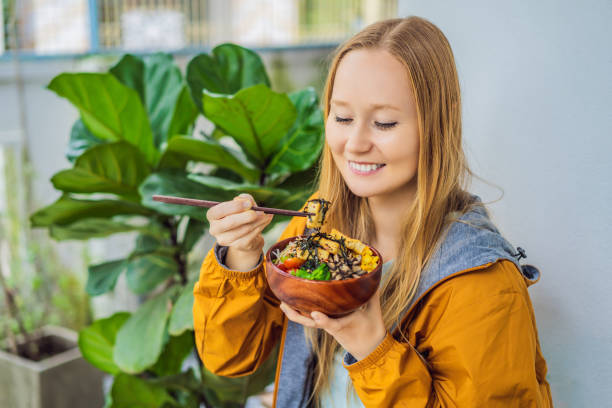 Woman eating Raw Organic Poke Bowl with Rice and Veggies close-up on the table. Top view from above horizontal stock photo