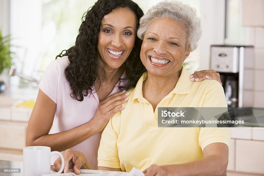 Mother and daughter in kitchen smiling Senior mother and adult daughter in kitchen with newspaper and coffee smiling Mother Stock Photo
