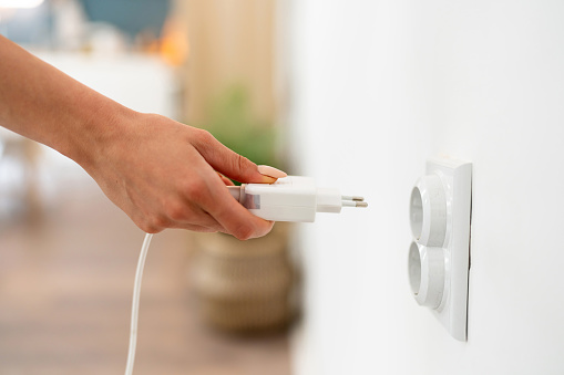 Woman's hand plugging cable in an electrical socket.