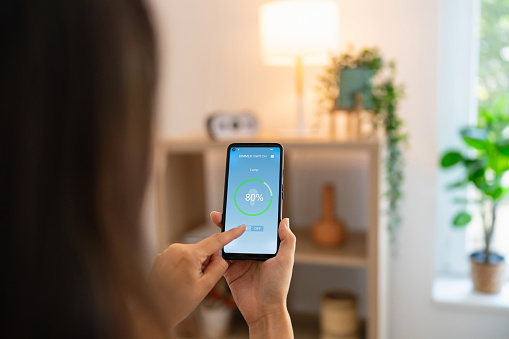 Woman controlling light with a smart phone at home.