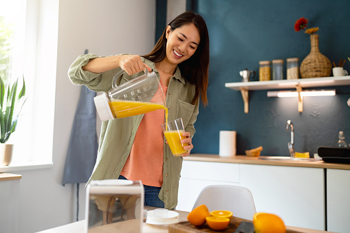 Woman pouring freshly-blended orange juice into drinking glass.