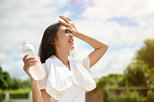 An exhausted Asian woman is fighting the heat wave while running in a park on a sunny day. An exhausted and sweaty young Asian woman in sportswear is fighting the heat wave while running in a park on a sunny summer day. summer activity, heat stroke, dehydrated young hot stock pictures, royalty-free photos & images
