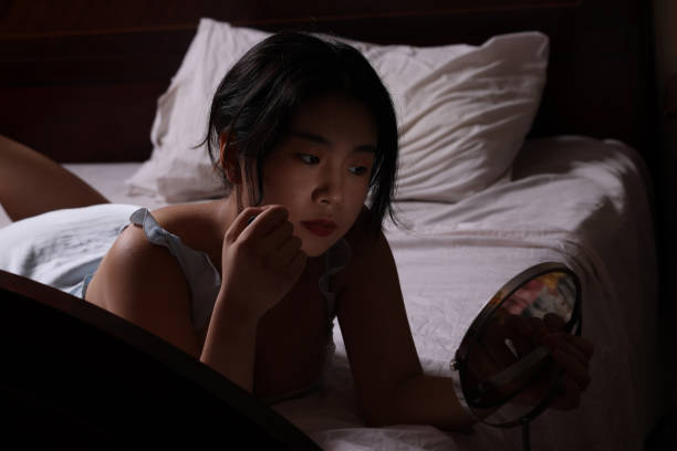 istock Young Chinese student laying in bed doing her make-up 1542320105