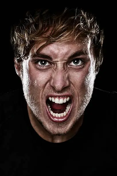 Man screaming angry aggressive at camera on black background. Young Caucasian mad male model. See more: