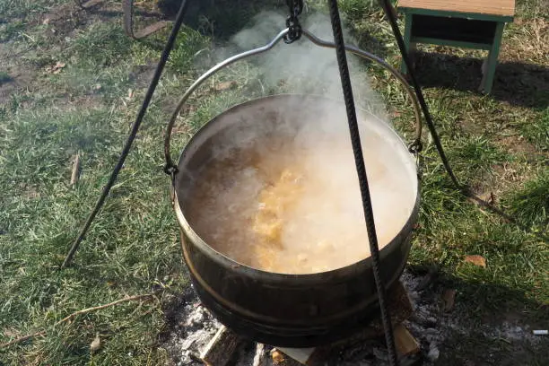 Cooking a traditional Serbian Balkan dish sauerkraut with smoked pork ribs and meat. Large cast iron vat cauldron. Delicious food gurgles and cooks on coals. Vegetables with meat are cooked on a fire