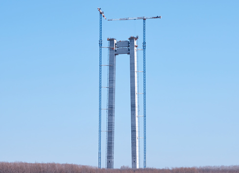 Tall concrete bridge pillars under construction with crane under blue sky