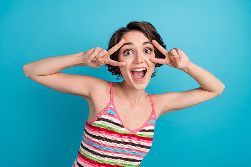 Photo of funky adorable woman dressed tank top showing two v-signs cover eyes isolated blue color background.