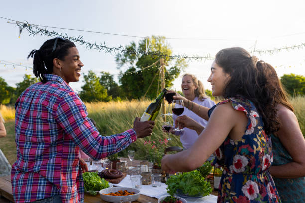 Cheers! Don't Drink Out of The Bottle Three friends are toasting each other , the two girls are using wine glasses the boy has a bottle, it is a summer evening and they are about to dine outside in a field, above them are hanging festive lights. dont eat meat stock pictures, royalty-free photos & images