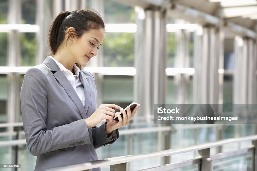 Businesswoman in suit using mobile phone in office building Hispanic Businesswoman Outside Office On Mobile Phone Smiling looking Down At phone Text Messaging Stock Photo