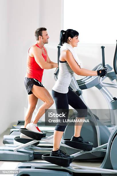 Man And Woman With Elliptical Cross Trainer At Gym Stock Photo - Download Image Now - 20-24 Years, 20-29 Years, 25-29 Years