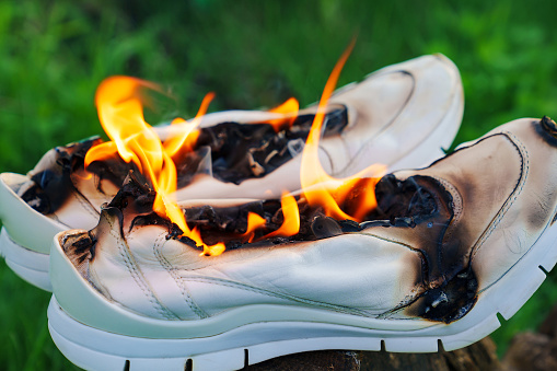 Burning white leather sports shoes. Sneakers or gym shoes on fire stand on the Stump in the meadow. athlete burned out in training. burnout from physical exertion, training