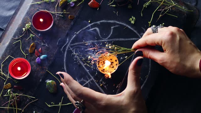 Witch hands burning herbs for a black magic ritual with the help of magical altar, candles and crystals