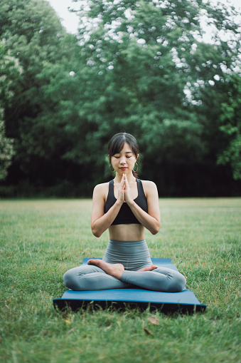 Beautiful Asian woman practicing yoga in a public park.