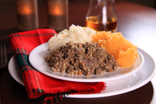 Scottish Haggis Serving For A Traditional Rabbie Burns Night Dinner With Neeps And Tatties A Glass Of Scotch Whiskey, Against A Royal Stuart Tartan Napkin