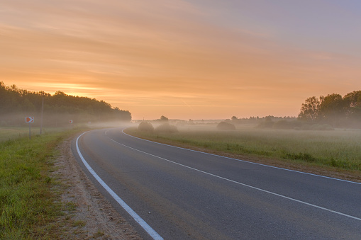 The asphalt road goes into the distance on a foggy summer morning. Beautiful foggy landscape.