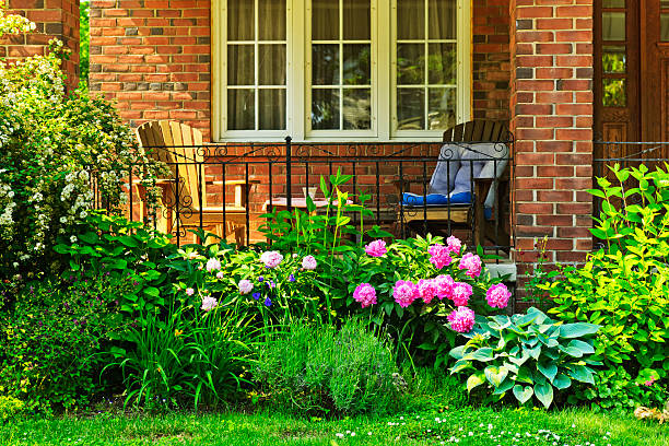 Garden growing below the front porch of a house Front of home with chairs and flower garden front porch stock pictures, royalty-free photos & images