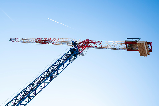 Close-up of a crane in white, red and blue. Sky with the wake of an aeroplane. Copy space on the sky