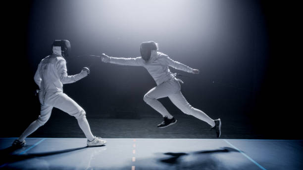 istock Two professional fencers foil swords dueling each other in combat with epic blue stage lighting and smoke effects. Jumping forward 1542471782