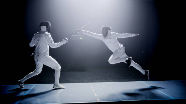 istock Two professional fencers foil swords dueling each other in combat with epic blue stage lighting and smoke effects. Jumping 1542472237