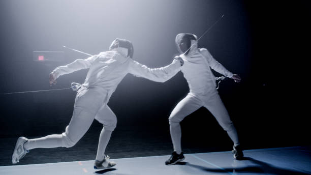 istock Two professional fencers foil swords dueling each other in combat with epic blue stage lighting and smoke effects. Landing a hit 1542472265