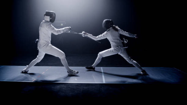 istock Two professional fencers foil swords dueling each other in combat with epic blue stage lighting and smoke effects. Ducking 1542472777