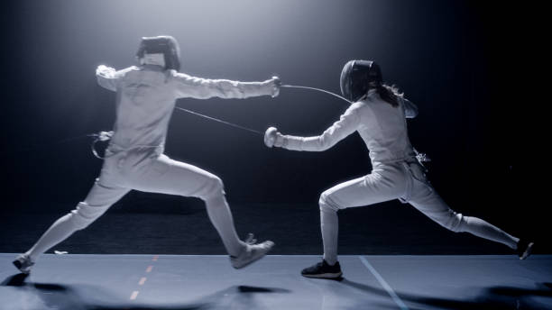 istock Two professional fencers foil swords dueling each other in combat with epic blue stage lighting and smoke effects. Ducking and dodging 1542472791